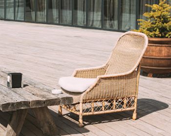Wicker Furniture On Balcony At Sunny Summer Day. Home Exterior With Chair And Wooden Table In A Wooden Terrace.
